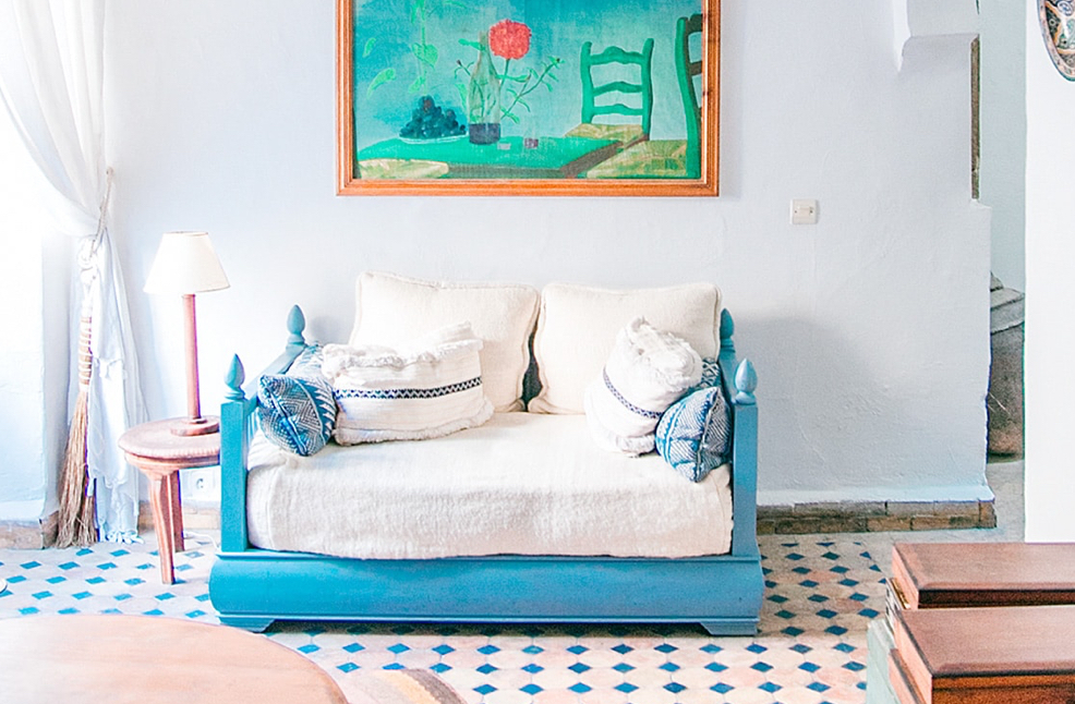 A blue sofa with pillows in a living room with a tile floor.