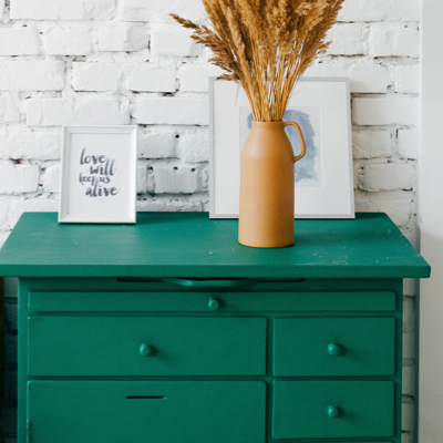 A green dresser with a clay picher full of dried grass.